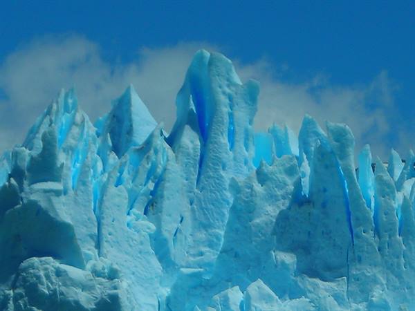 Blue ice pinnacles of Perito Moreno glacier beneath white clouds