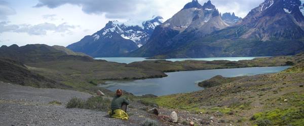 Hiker sitting on green rock by turquoise lake beneath Torres del Paine peaks