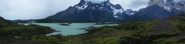 Turquoise lake beneath snow-capped peaks of Torres del Paine, green hills