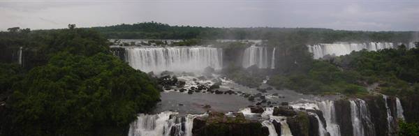 Iguazú Falls amid green forest, water cascades and rocks under gray sky