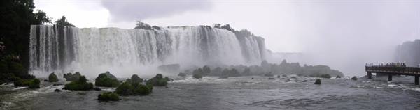 Iguazú Falls: powerful cascades over mossy rocks, walkway with visitors under a grey sky