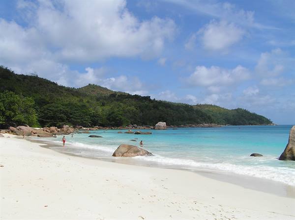 White sand beach with granite boulders, turquoise water and swimmers, tropical greenery
