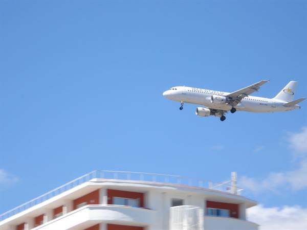 White airplane landing above a building with balconies, blue sky