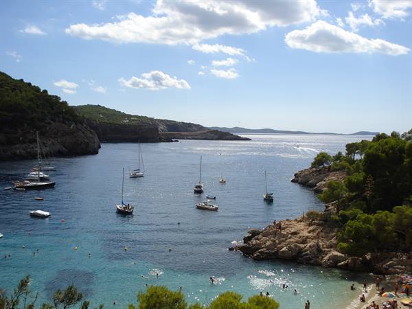 Sailboats anchored in turquoise cove with rocks, pines and swimmers