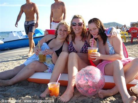 Three girls in bikinis sitting on the beach with drinks and pink ball