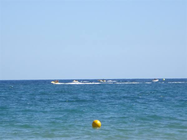 Jet skis and boats speed across blue sea, yellow buoy in foreground