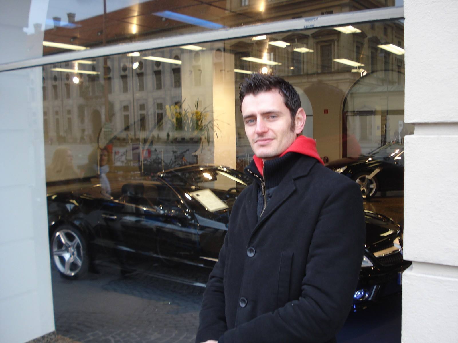 Man in black coat with red hood outside a Mercedes dealership showroom window