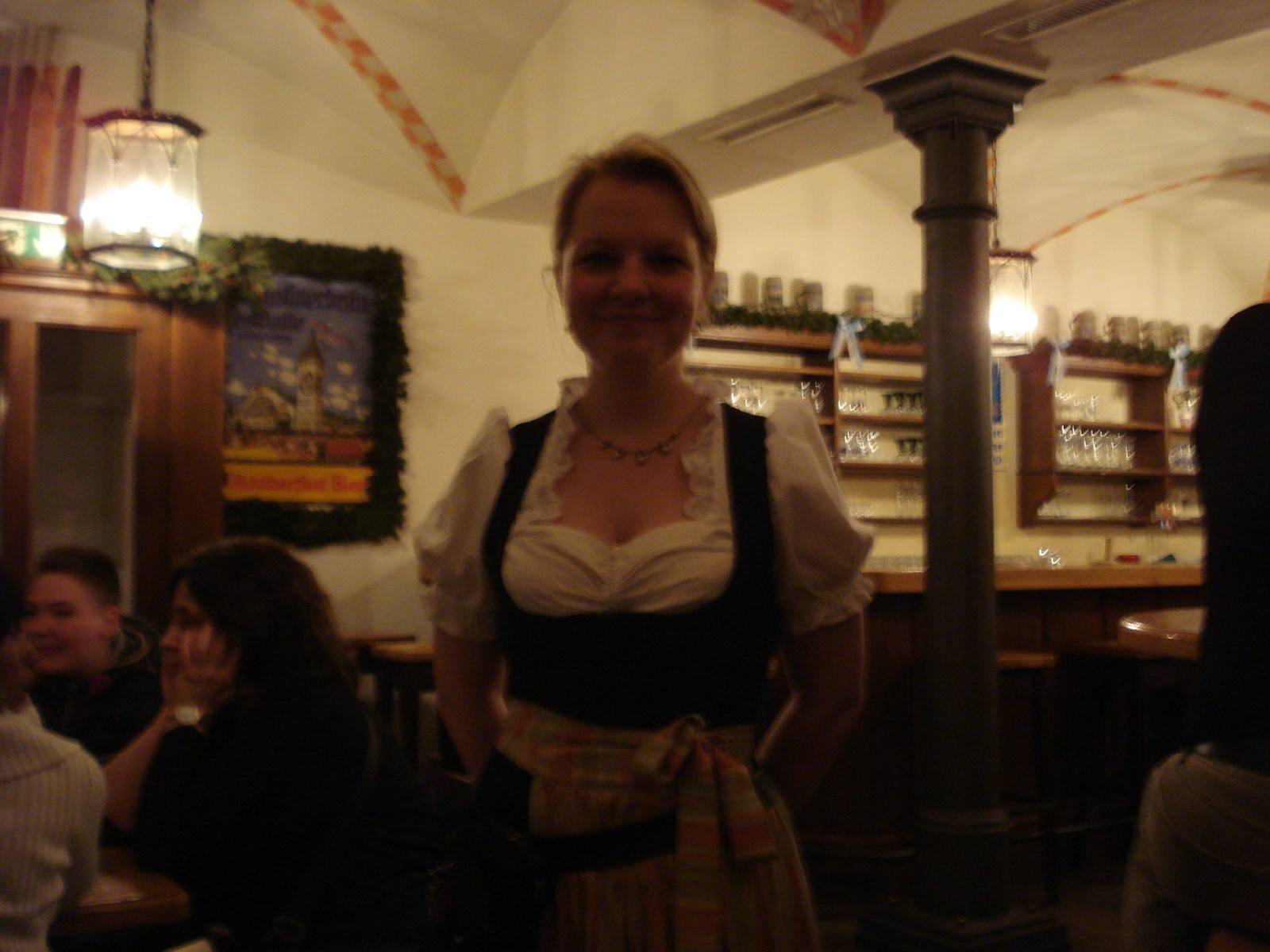 Smiling waitress in dirndl inside Hofbräuhaus beer hall, glowing lanterns and wooden counters