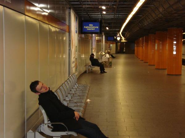 Man sleeping on a metal seat in a subway station with orange columns