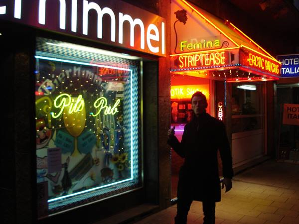 Man in coat outside pub and clubs with neon signs at night