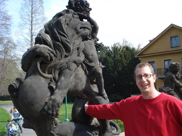 Tourist in red sweater next to a stone crowned lion statue in the park