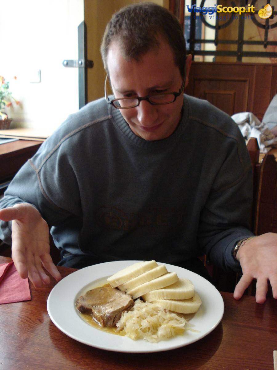 Man with glasses at restaurant facing plate of sauerkraut, meat and dumplings