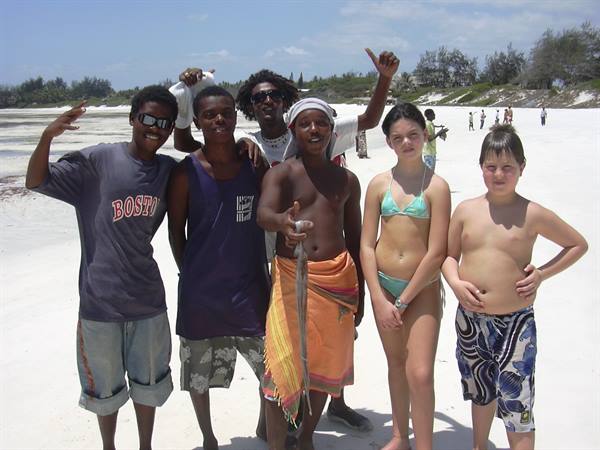 Teens pose on white sand beach, one holding up a freshly caught fish