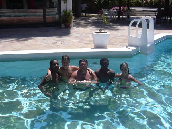Five friends in an outdoor pool, bright sunlight on the blue water