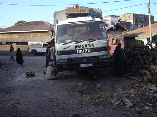 White Isuzu truck parked on dirt road, men nearby, wooden buildings