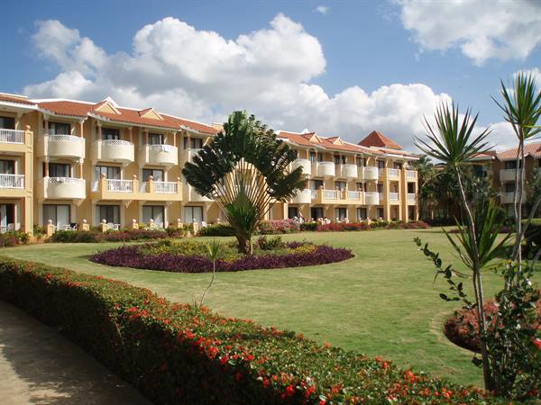 White-balconied hotel with red roofs in front of flowering garden and palms