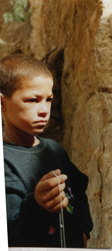 Boy in dark sweatshirt holding a string, sunlit stone wall behind