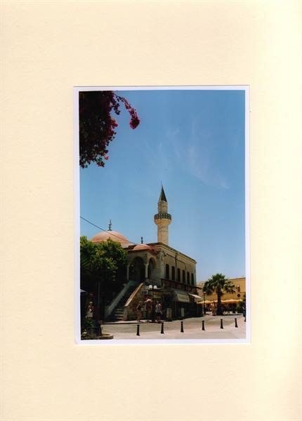 Stone mosque with minaret, sunny square with palm trees and bougainvillea