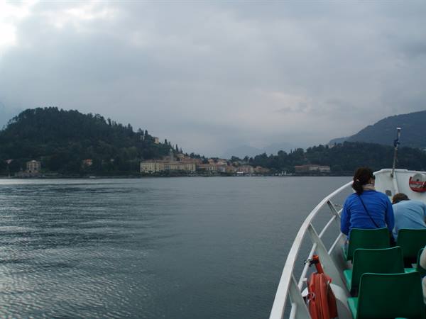Tourist on ferry boat looking at shoreline villas and green hill, cloudy sky
