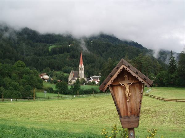 Wooden wayside shrine with crucifix in a meadow, church and foggy wooded hills