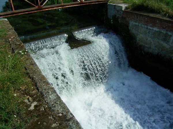 Foamy water cascading from a concrete weir beneath a rusty metal bridge