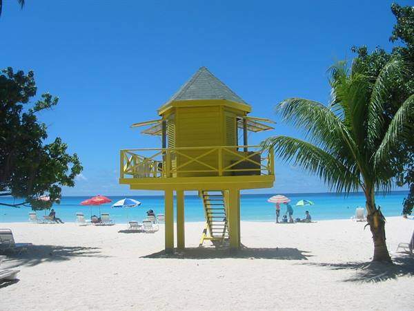 Yellow lifeguard tower on white sand, umbrellas and palm by the turquoise sea