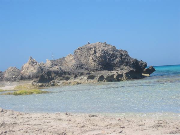 Large dark rock on sandy beach, clear turquoise water