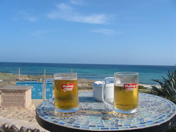Two Mahou beer mugs on a mosaic table in front of the sea