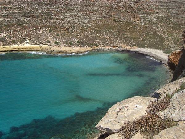 Rocky cove with clear turquoise water, limestone cliffs and sandy beach under sun