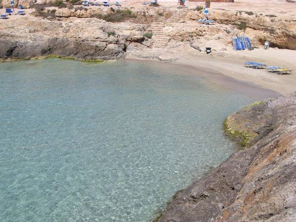 Rocky cove with clear turquoise water, sandy beach and sun loungers