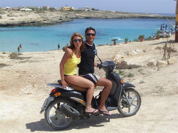 Couple on a scooter in front of a turquoise cove in Lampedusa