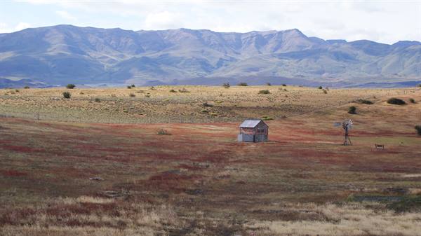 Wooden cabin and windmill among red shrubs, blue mountains behind