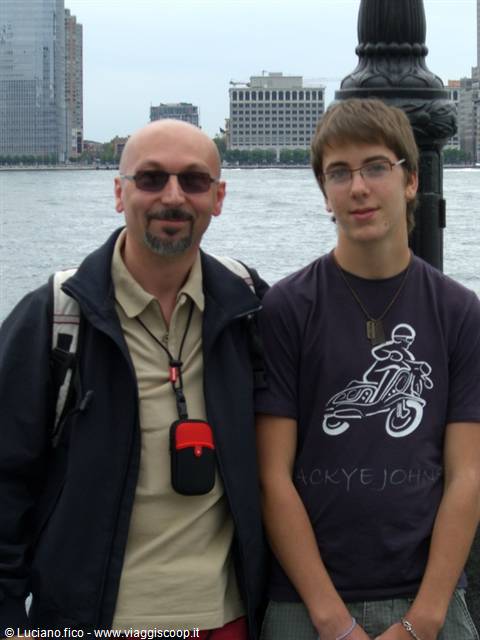 Father and son pose by the Hudson River, Manhattan skyscrapers behind them