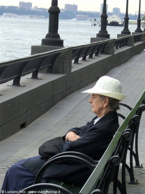 Woman in white hat sitting on a bench along the Hudson River, New York
