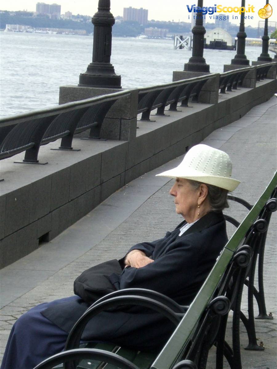 Woman in white hat sitting on a bench along the Hudson River, New York