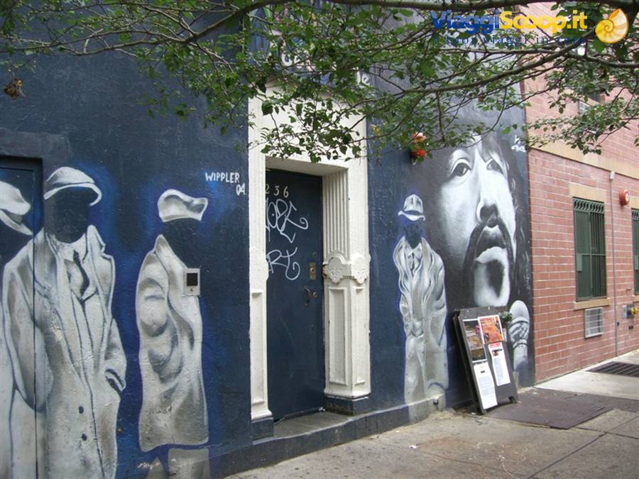 Mural of male portraits on blue wall beside a doorway, tree branches above