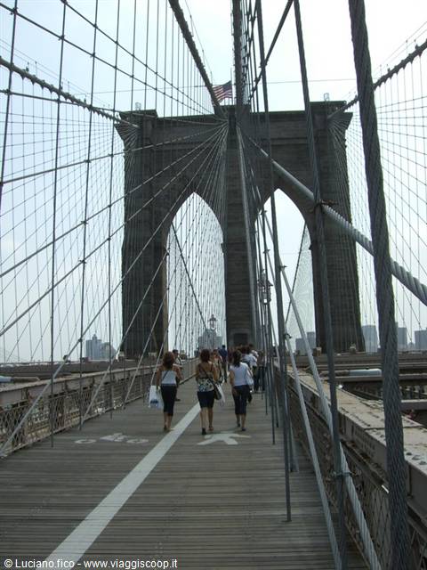 Tourists walk on the Brooklyn Bridge wooden walkway among steel cables
