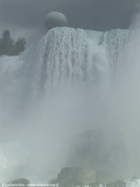 Powerful waterfall with water mist, rocks and grey sky above