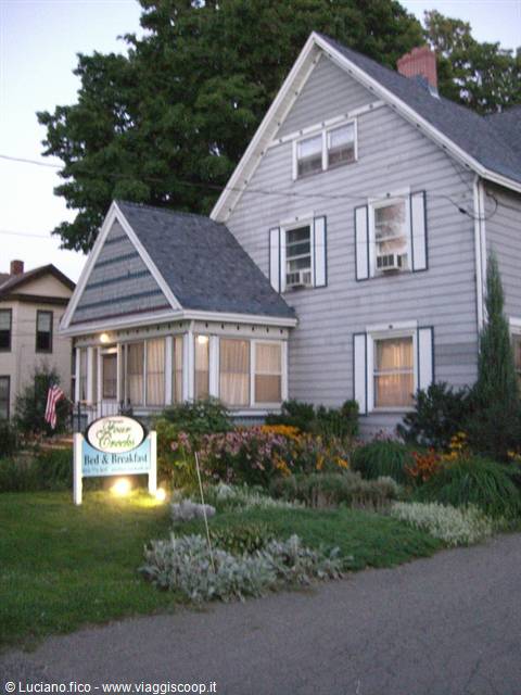 Gray wooden house with porch and bed and breakfast sign among flowers