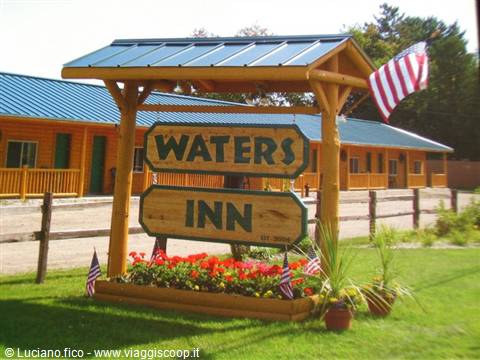 Wooden Waters Inn sign with red flowers, American flag and log motel