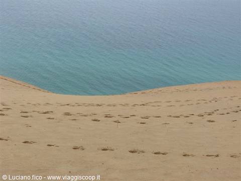 Footprints on sand dunes facing a turquoise sea