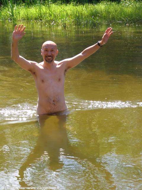 Shirtless man raising both arms while bathing in green water