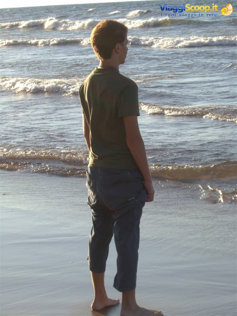 Barefoot boy in green shirt watching waves roll onto the shore