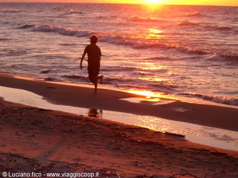 Child running on wet sand at sunset, glowing sea waves