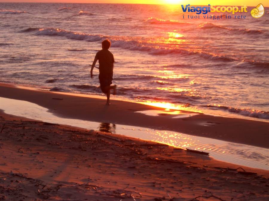 Child running on wet sand at sunset, glowing sea waves