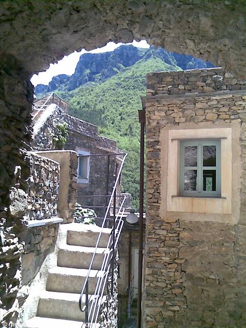 Stone stairs under an arch between stone houses and green mountain