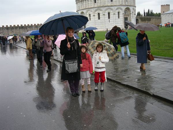 Mother and two girls with umbrellas in the rain by Pisa Baptistery