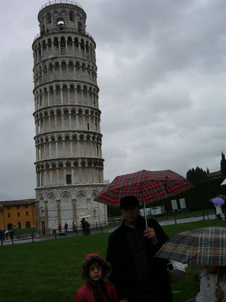 Tourists with umbrellas under the Leaning Tower of Pisa on a gray day