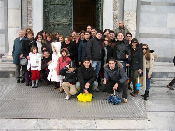 Group of tourists in winter jackets posing before Pisa Cathedral's bronze door