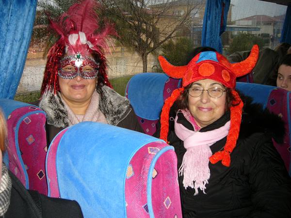 Two women wearing feather mask and red horned hat inside a bus in Viareggio